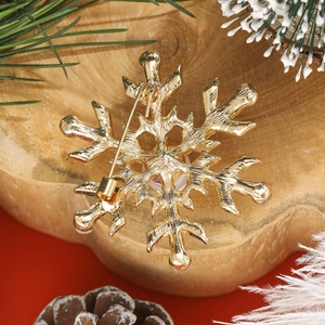 Broche flocon de neige dorée avec épingle de sûreté sur fond de Noël festif et bois