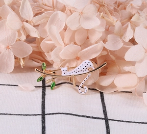 Détail de broche chat blanc peint à la main sur une branche dorée avec feuilles vertes