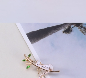 Détail de la broche léopard peinte à la main sur une branche dorée et feuilles vertes