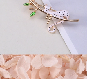 Détail d'une broche léopard sur branche dorée avec feuilles en émail vert brillant