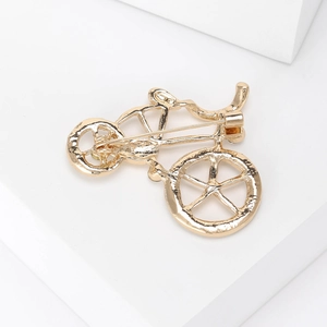 Close-up of golden bicycle brooch showing metal frame and secure pin clasp on the back