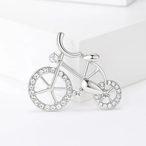 Silver bicycle brooch with sparkling white crystals on a white geometric stand