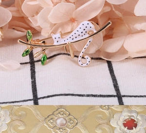 Détail d'une broche chat sur une branche dorée avec des feuilles d'émail vert
