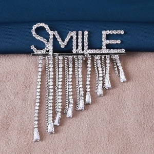 Détail de la broche SMILE argentée avec chaînes à pompons et strass étincelants