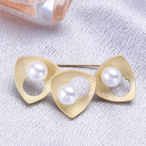 Detail of gold brushed metal brooch with three freshwater pearls on grey fabric texture