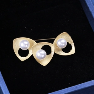 Detail of minimalist gold brooch with three pearls and brushed metal finish on black velvet