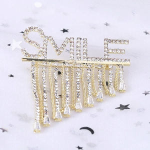 Détail de la broche SMILE dorée avec des pompons en cristal scintillant et strass