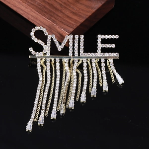 Détail d'une broche dorée SMILE avec glands en zircon étincelants sur fond noir élégant