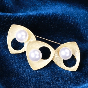 Detailed macro view of brushed gold triangular brooch with three elegant white pearls