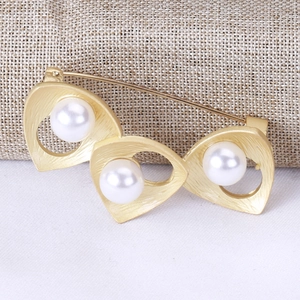 Detailed macro view of gold-plated pearl brooch featuring matte finish and safety pin clasp