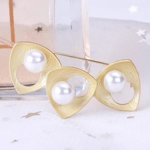 Detail of golden geometric brooch featuring brushed metal triangles and three white pearls