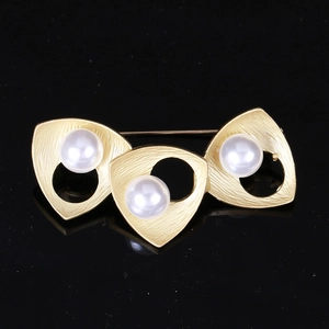 Detail of matte gold geometric brooch with natural freshwater pearls on a black surface