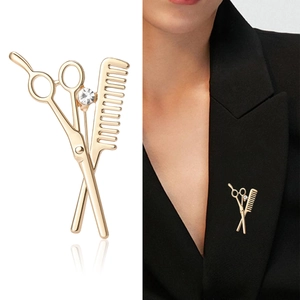 Golden scissors and comb brooch with rhinestone on black suit lapel and white background