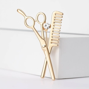 Detail of gold scissor and comb brooch with a sparkling gemstone on white display stand