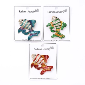 Détail de trois broches poisson en émail avec strass étincelants sur cartes blanches