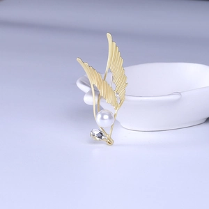 Close-up of golden wing brooch with pearl and diamond detail on white plate