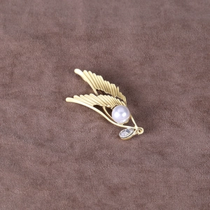 Macro shot of matte gold angel wing brooch with a white pearl and teardrop zircon