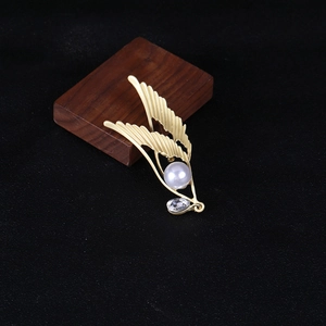 Detail of matte gold angel wing brooch with a large pearl and teardrop zircon pendant