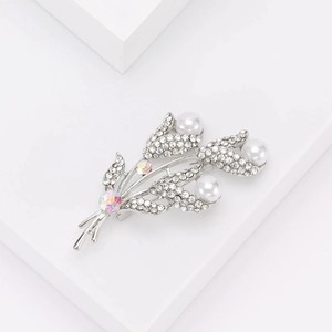 Broche fleur argentée avec perles blanches et strass brillants sur fond blanc épuré