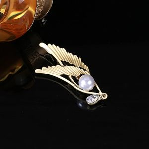 Detail of matte gold angel wing brooch featuring an elegant pearl and teardrop zircon