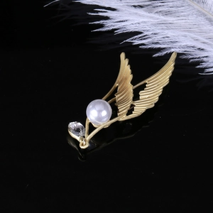 Close-up of matte gold angel wing brooch with central pearl and sparkling zircon stone