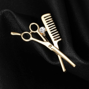 Detailed view of gold scissors and comb brooch with rhinestone on black leather background
