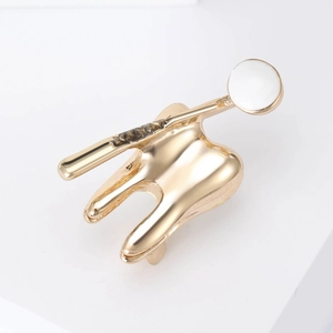 Vue détaillée de la broche créative dorée en forme de dent et miroir dentaire