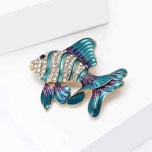 Vue macro d'une broche poisson tropical en émail dégradé bleu et strass sur cubes blancs