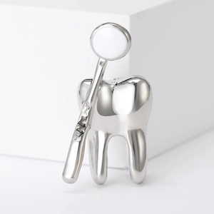 Macro d'une broche argentée en forme de dent et miroir dentaire sur fond blanc minimaliste