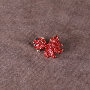 Gros plan sur la broche carpe koi en cristal rouge avec yeux en gemmes vertes sur velours
