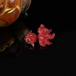 Vue détaillée d'une broche carpe avec strass rouges et détails dorés sur fond noir brillant