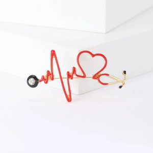 Détail de la broche stéthoscope dorée avec cœur en émail rouge et ligne d'électrocardiogramme
