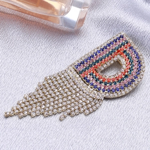 Spilla scintillante a forma di D con strass colorati e nappe metalliche pendenti