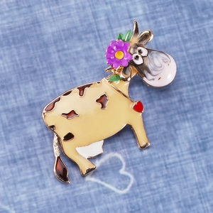 Detailed view of enamel cow brooch with flower decor on blue fabric background