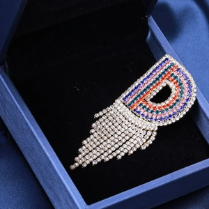 Dettaglio della spilla a lettera D con strass arcobaleno e nappe di cristallo pendenti
