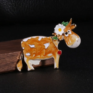 Detail of enameled cow brooch with marble texture and floral accents on wood
