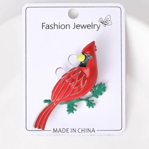 Detail of red cardinal enamel brooch on a display card with golden branch accents