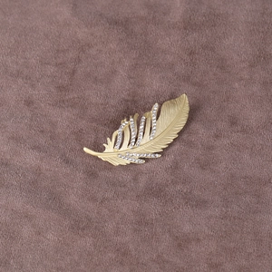 Détail d'une broche plume en or mat avec des strass blancs fins sur fond en velours