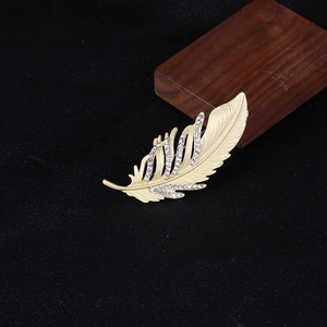 Détail macro d'une broche plume dorée avec zircons et texture métallique brossée