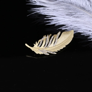 Détail de la broche plume en or mat avec diamants incrustés sur surface réfléchissante