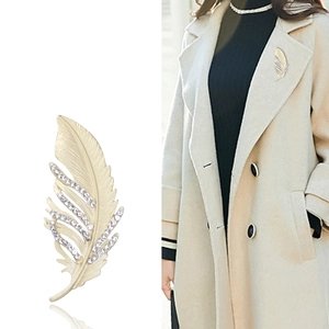 Broche plume dorée mate avec cristaux présentée sur mannequin et fond blanc pur
