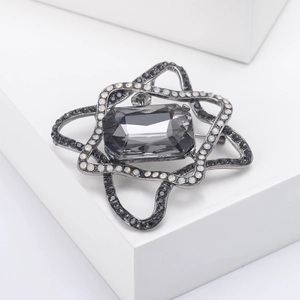 Detail of vintage starburst brooch with grey crystal and black rhinestones on white stand