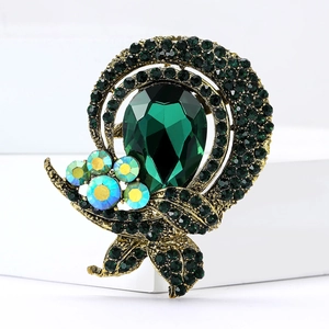 Detail of vintage emerald crystal brooch with gold leaf design on white stand