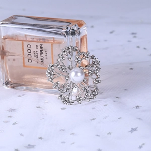 Macro view of silver floral brooch with pearls and rhinestones on soft white mesh background