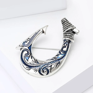 Vintage silver fish hook brooch with blue enamel scrollwork on a white podium