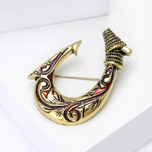 Macro detail of vintage gold fish hook brooch with red enamel and cord texture