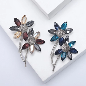 Detailed macro view of two crystal flower brooches in blue and red on white stone