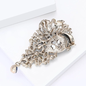 Vintage gold crystal brooch with blue teardrop pendant shown on a white background