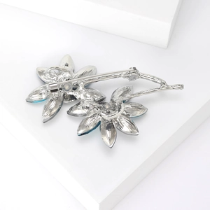 Elegant floral brooch with blue crystal petals and silver metal finish on white stand
