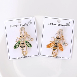 Gros plan de broches abeilles dorées avec ailes en émail et strass sur plat blanc